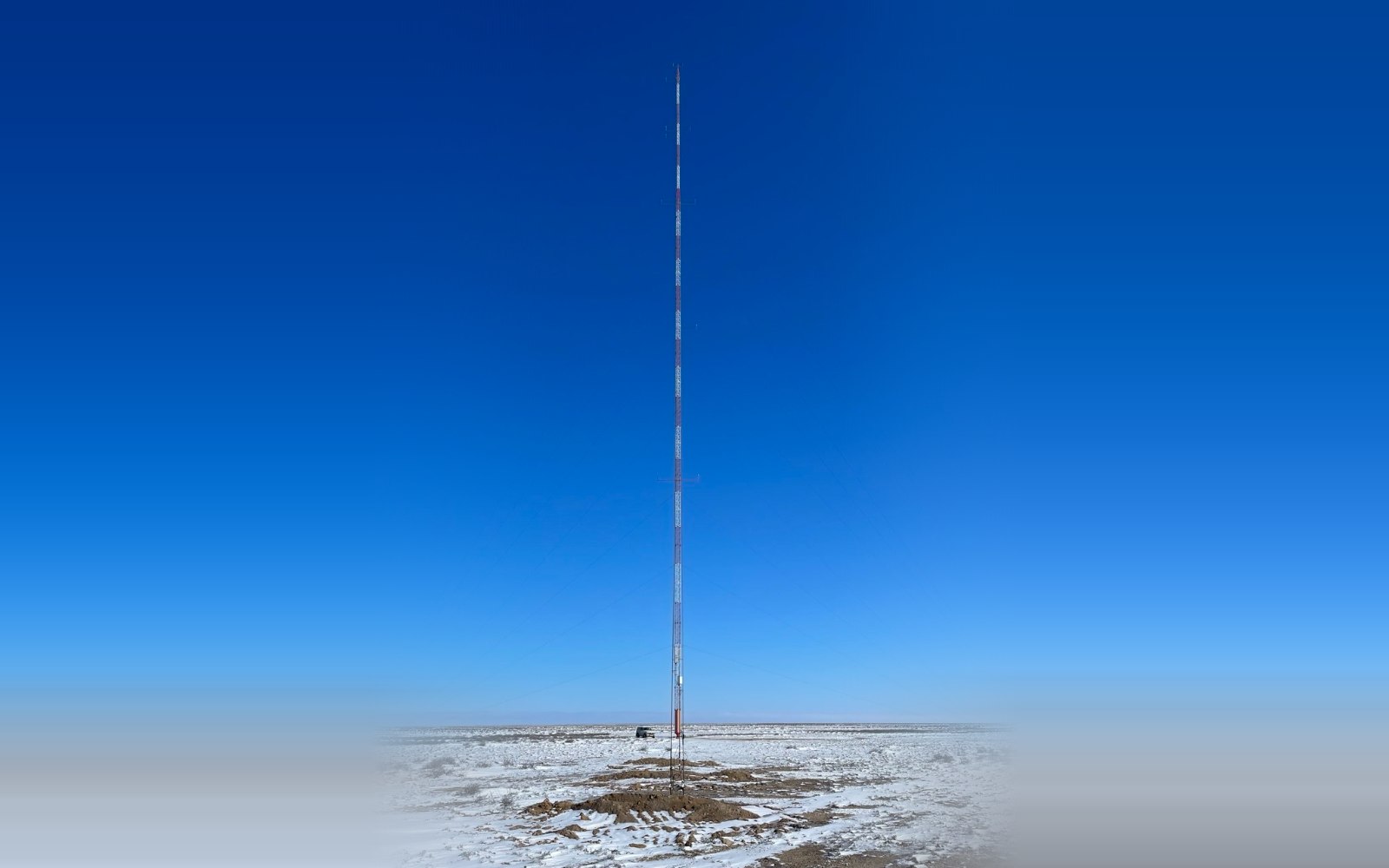 A tall guyed met mast in snow-covered steppe under a clear winter sky